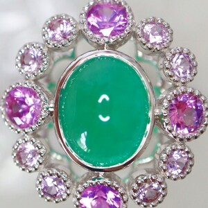 May include: A silver ring with a green oval gemstone surrounded by a halo of smaller purple gemstones.