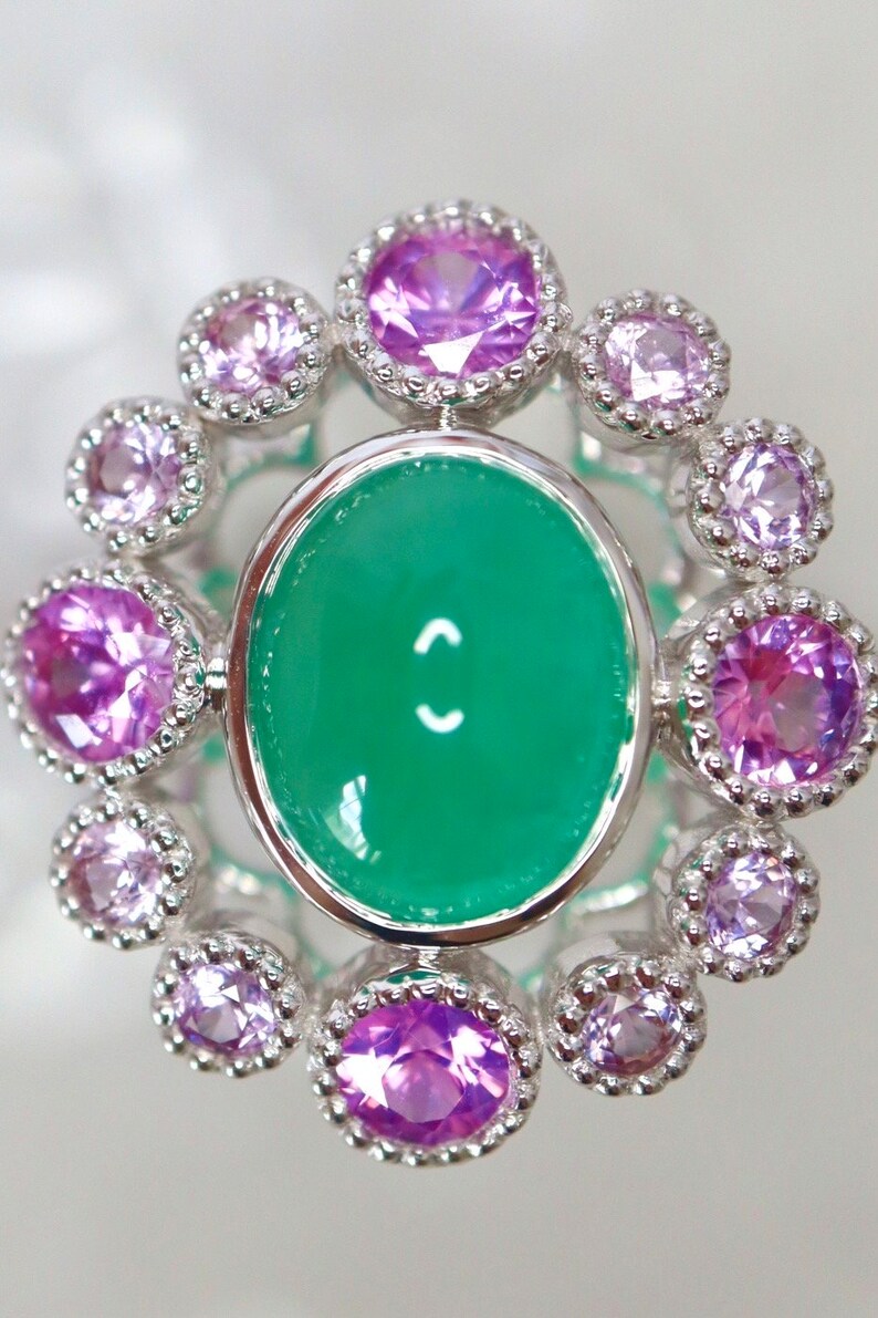 May include: A silver ring with a green oval gemstone surrounded by a halo of smaller purple gemstones.