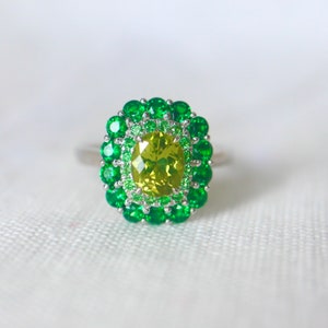 May include: A ring with a large, oval-shaped, yellow-green gemstone surrounded by two rows of smaller, green gemstones.