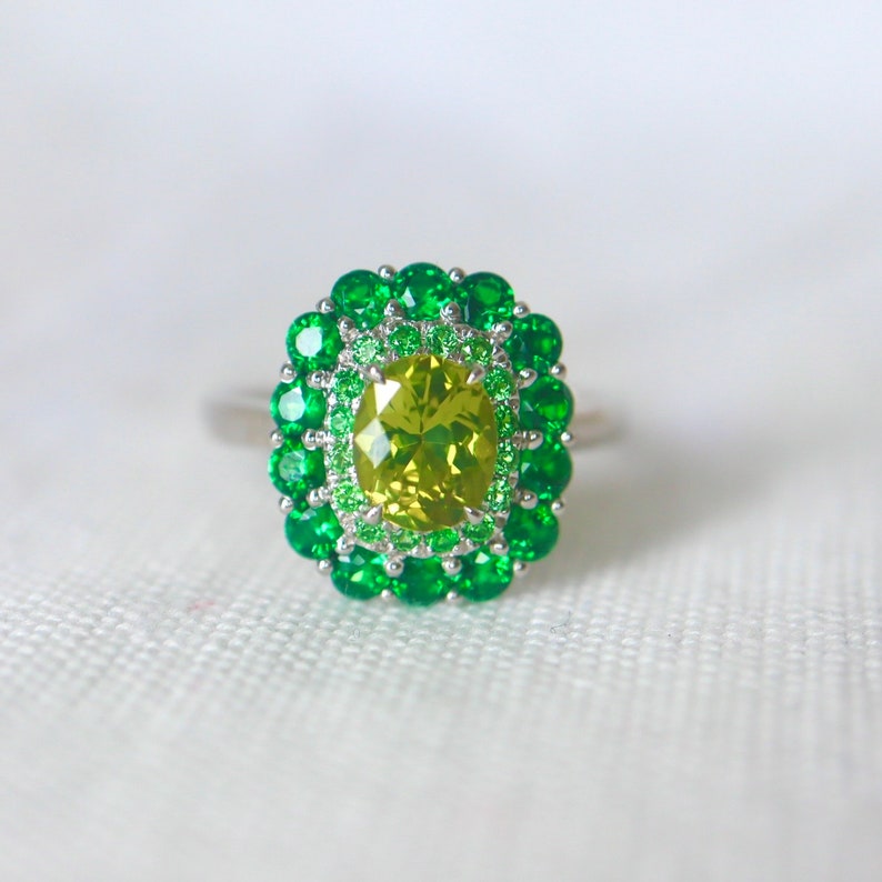 May include: A ring with a large, oval-shaped, yellow-green gemstone surrounded by two rows of smaller, green gemstones.