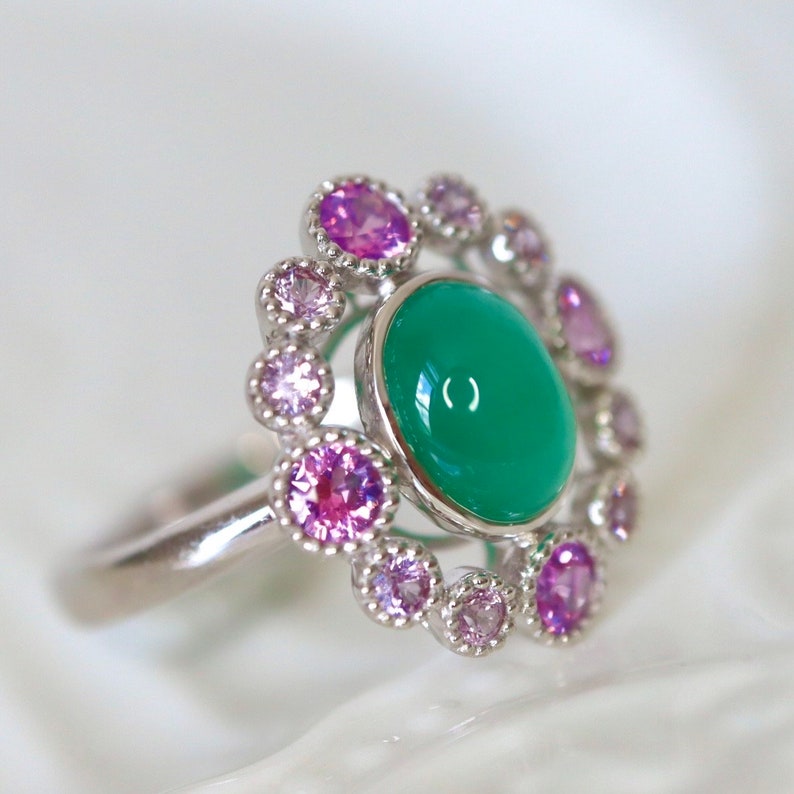 May include: A silver ring with a green gemstone surrounded by a halo of pink gemstones.