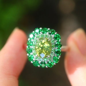 May include: A ring with a large, oval-shaped, light green gemstone surrounded by a double halo of smaller green gemstones.