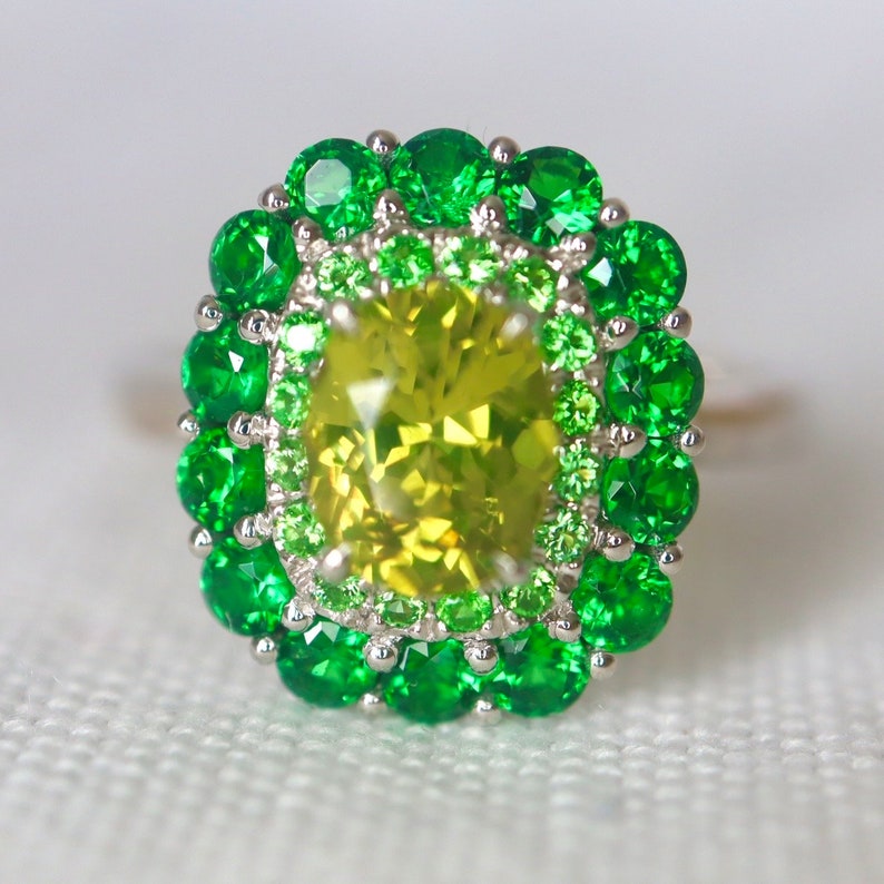 May include: A ring with a large, yellow-green gemstone surrounded by two rows of smaller, green gemstones.