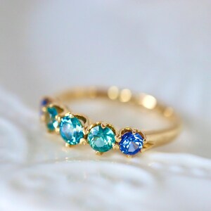May include: A gold band ring with five blue gemstones. The gemstones are set in a curved line and are different shades of blue.