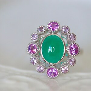 May include: A silver ring with a large green oval gemstone surrounded by a halo of smaller pink gemstones.