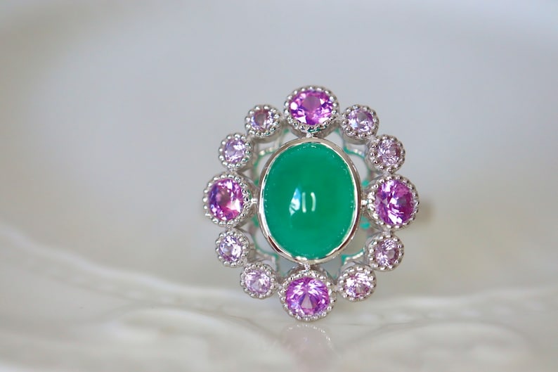 May include: A silver ring with a large green oval gemstone surrounded by a halo of smaller pink gemstones.
