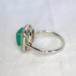 May include: A silver ring with a green gemstone set in a delicate, intricate design. The ring has a polished finish and a simple band.