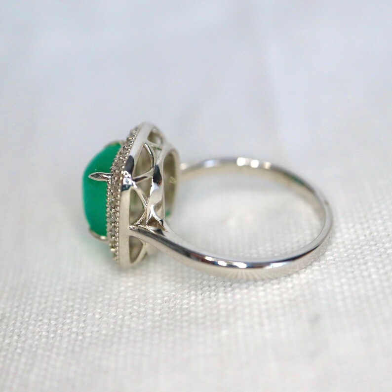 May include: A silver ring with a green gemstone set in a delicate, intricate design. The ring has a polished finish and a simple band.