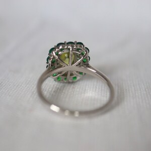 May include: A silver ring with a large green gemstone surrounded by smaller green gemstones.