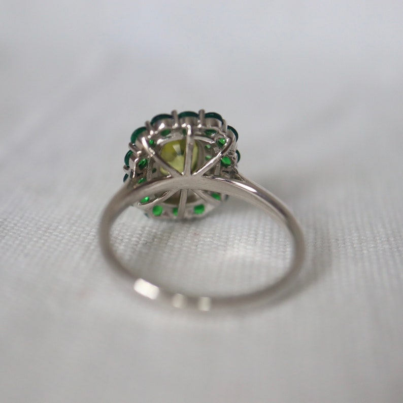 May include: A silver ring with a large green gemstone surrounded by smaller green gemstones.