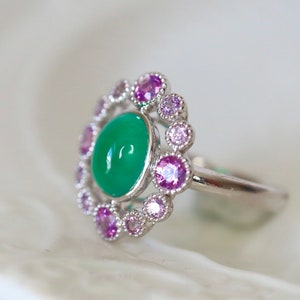 May include: A silver ring with a green gemstone surrounded by a halo of smaller pink and purple gemstones.