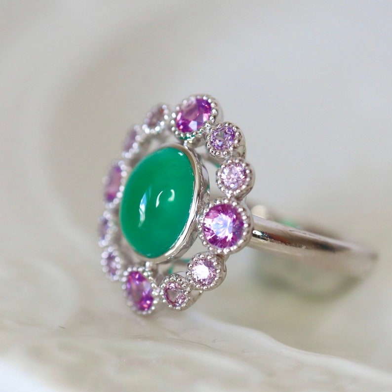 May include: A silver ring with a green gemstone surrounded by a halo of smaller pink and purple gemstones.