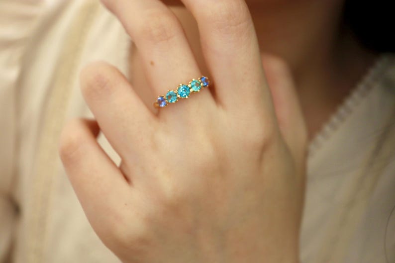 May include: A gold ring with a row of blue and turquoise gemstones.