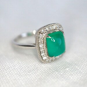 May include: A silver ring with a square green gemstone surrounded by a halo of small diamonds.