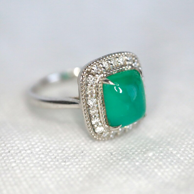 May include: A silver ring with a square green gemstone surrounded by a halo of small diamonds.