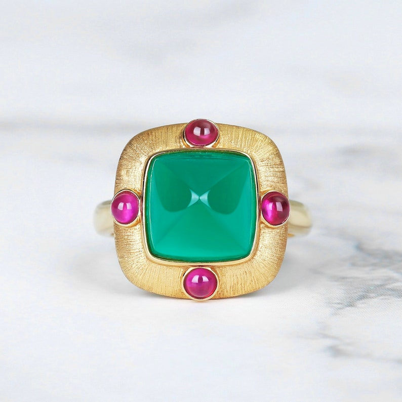 May include: A gold ring featuring a square green gemstone surrounded by four smaller pink gemstones.