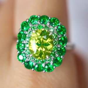 May include: A ring with a large, yellow-green gemstone surrounded by a double halo of smaller green gemstones.