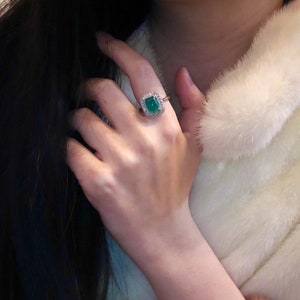 May include: A ring with a large, emerald green gemstone surrounded by smaller, clear gemstones. The ring is set in a gold band.