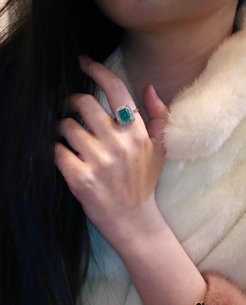 May include: A ring with a large, emerald green gemstone surrounded by smaller, clear gemstones. The ring is set in a gold band.