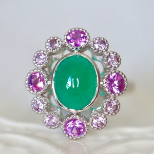 May include: A silver ring with a green oval gemstone surrounded by a halo of smaller pink gemstones.