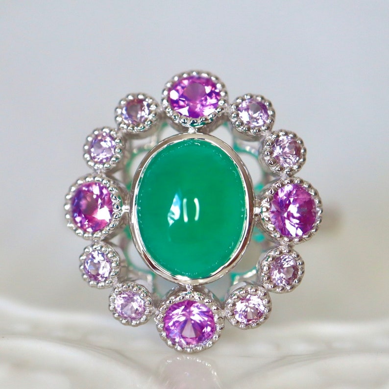 May include: A silver ring with a green oval gemstone surrounded by a halo of smaller pink gemstones.
