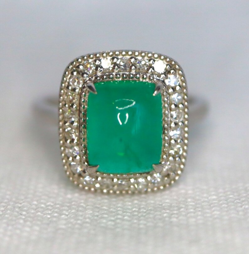 May include: A silver ring with a large, square, green gemstone surrounded by a halo of smaller, white gemstones.