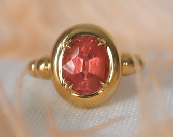 Puede incluir: Un anillo de oro con una gran piedra preciosa rosa de forma ovalada facetada engastada en un engaste de bisel.