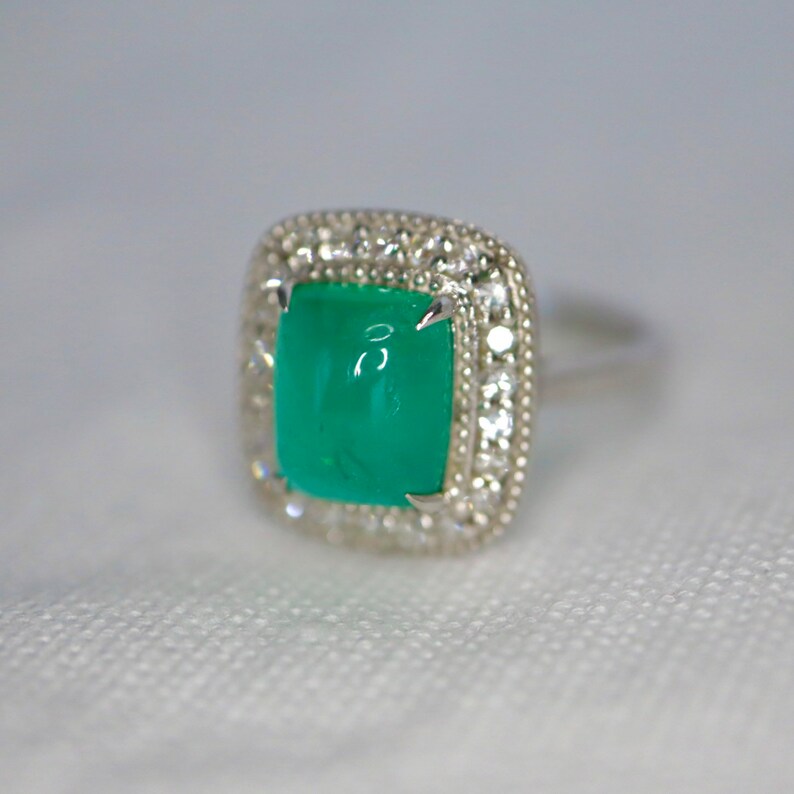 May include: A silver ring with a square emerald green gemstone surrounded by a halo of smaller clear gemstones.