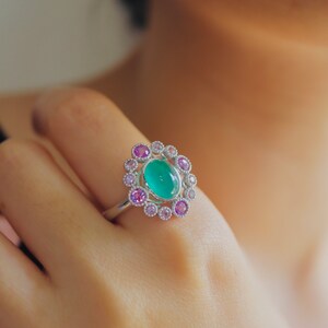 May include: A silver ring with a green oval gemstone surrounded by a halo of smaller pink and white gemstones.