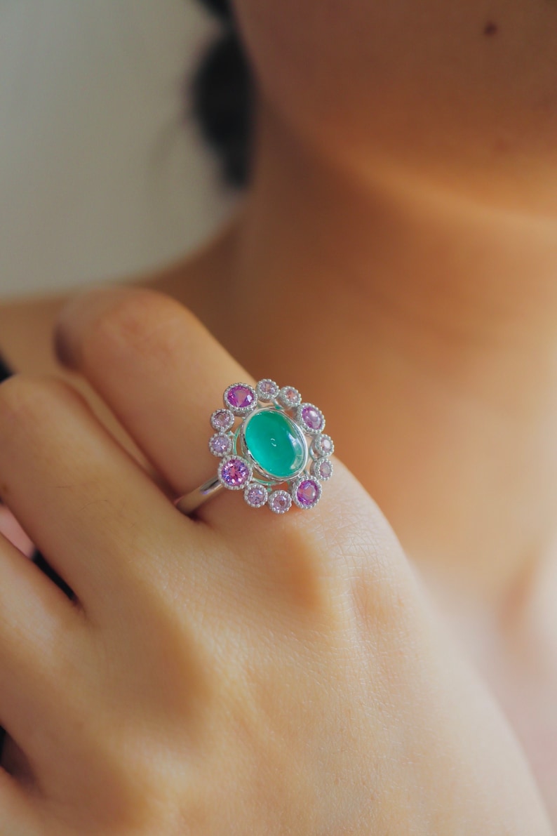 May include: A silver ring with a green oval gemstone surrounded by a halo of smaller pink and white gemstones.