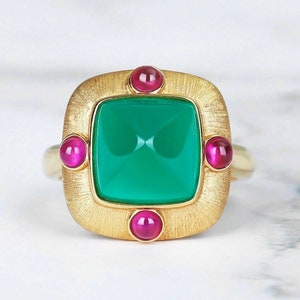 May include: A gold ring featuring a square green gemstone surrounded by four smaller pink gemstones.