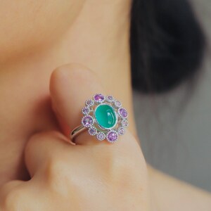 May include: A silver ring with a green oval gemstone surrounded by a halo of smaller pink gemstones.