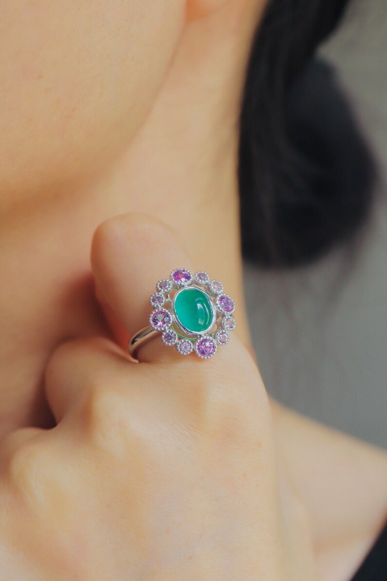 May include: A silver ring with a green oval gemstone surrounded by a halo of smaller pink gemstones.