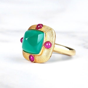 May include: A gold ring featuring a square green gemstone surrounded by four smaller pink gemstones.
