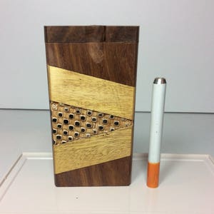 May include: A rectangular wooden box with a geometric design, featuring dark brown and light brown wood with a gold-colored accent. A white and orange cigarette is next to the box.