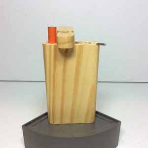 May include: A wooden box with a built-in pipe and a small orange tube. The box is sitting on a gray, curved base.