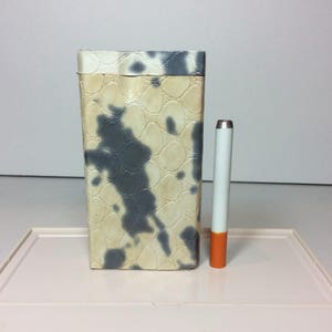 May include: A white and gray patterned metal container with a cigarette-sized object next to it.