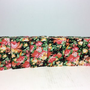 Puede incluir: Seis peque&ntilde;as cajas negras con un patr&oacute;n floral en tonos rojos, naranjas, amarillos y verdes. Las cajas est&aacute;n alineadas en una fila.