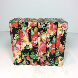 Puede incluir: Ocho cajas negras con un patr&oacute;n floral en tonos rojos, amarillos y verdes. Las cajas est&aacute;n alineadas en una fila.