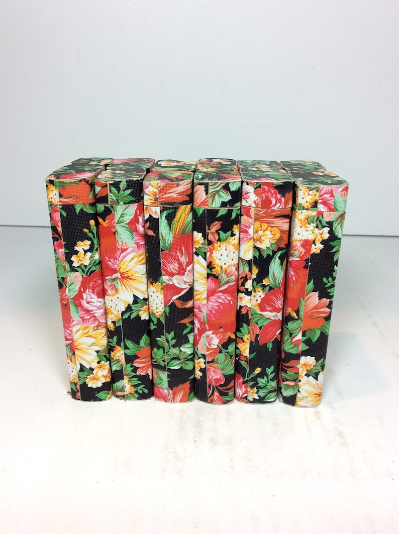Puede incluir: Ocho cajas negras con un patr&oacute;n floral en tonos rojos, amarillos y verdes. Las cajas est&aacute;n alineadas en una fila.