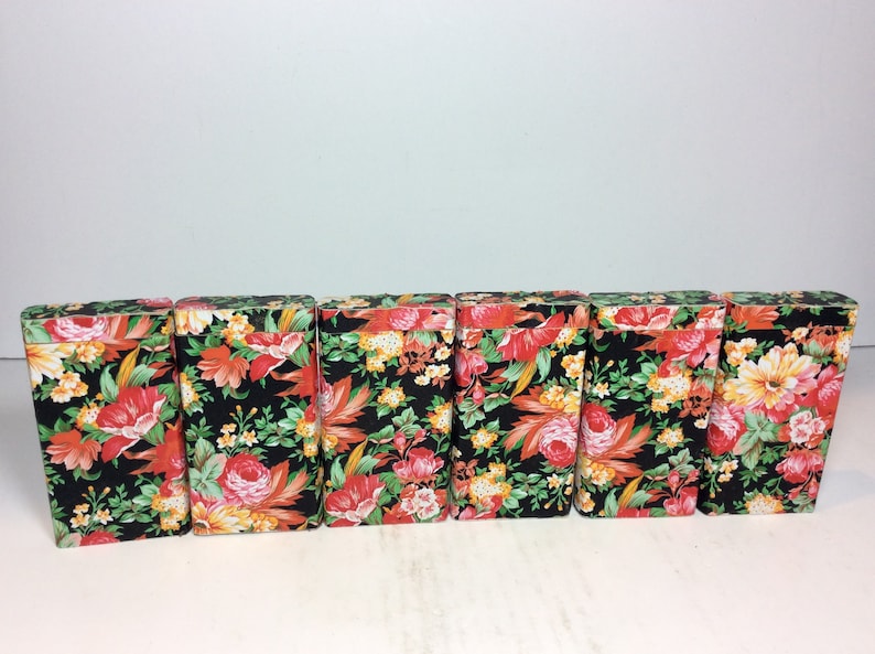 Puede incluir: Seis peque&ntilde;as cajas rectangulares con motivos florales. Las cajas son negras con flores rojas, naranjas, amarillas y verdes.
