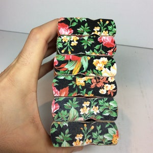 Puede incluir: Un conjunto de seis pinzas de madera con un patr&oacute;n floral. Las pinzas son negras con flores rojas, amarillas y verdes.