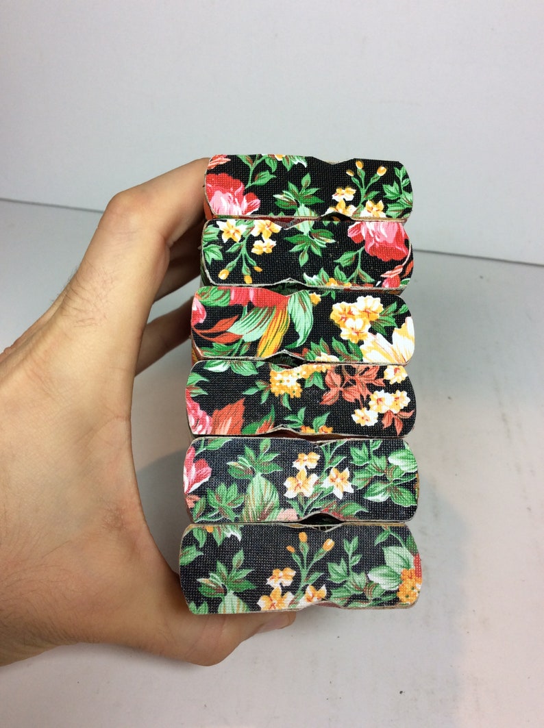 Puede incluir: Un conjunto de seis pinzas de madera con un patr&oacute;n floral. Las pinzas son negras con flores rojas, amarillas y verdes.