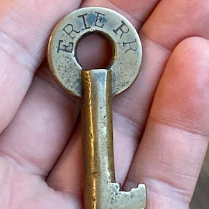 May include: A brass key with a round head that says "ERIE RR" on it. The key has a worn, antique look.
