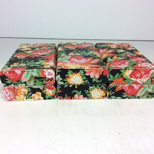 Puede incluir: Tres cajas apiladas con un patr&oacute;n floral. Las cajas son negras con flores rojas, naranjas, amarillas y blancas.