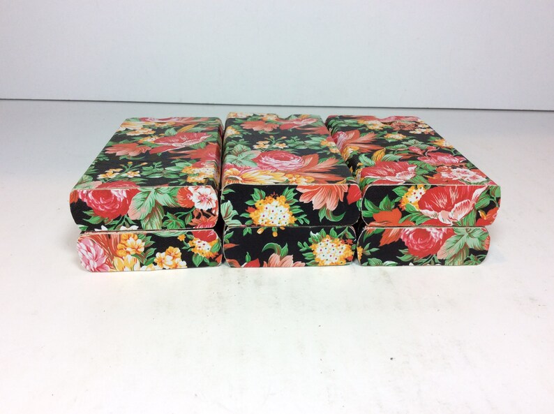 Puede incluir: Tres cajas apiladas con un patr&oacute;n floral. Las cajas son negras con flores rojas, naranjas, amarillas y blancas.