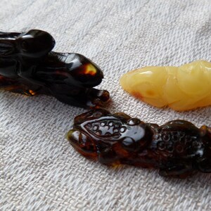 May include: Three amber carvings of animals: a rabbit, a frog, and a fish. The rabbit and frog are dark amber, while the fish is a lighter yellow amber.