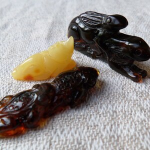 May include: Three amber animal figurines: a yellow frog, a brown dragon, and a black rabbit riding another rabbit.