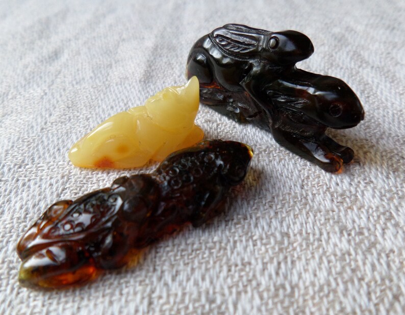 May include: Three amber animal figurines: a yellow frog, a brown dragon, and a black rabbit riding another rabbit.