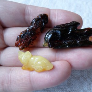 May include: Three amber carvings of animals. A brown and black rabbit, a brown and black dragon, and a yellow cat.